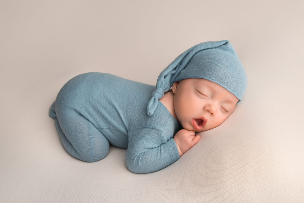 baby boy in blue sleeper and cap sleeps with mouth open during Las Vegas Studio newborn portraits